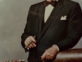 Movie still from “Gates of Heaven” (1978), directed by Errol Morris – An older man wearing a suit and bow tie holding a pen; Extreme Close Up shot, Overhead angle