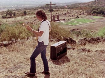 Movie still from “Gates of Heaven” (1978), directed by Errol Morris – A man standing on top of a grass covered hill; Wide shot, High angle