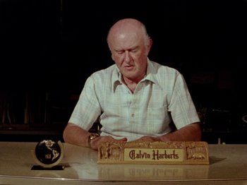 Movie still from “Gates of Heaven” (1978), directed by Errol Morris – An older man sitting at a table with a clock; Medium shot, Low angle