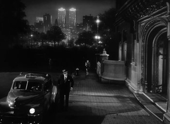 Movie still from “Gentleman's Agreement” (1947), directed by Elia Kazan – A black and white photo of a man standing next to a car in front of a building; Extreme Wide shot, High angle