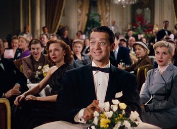 Movie still from “Gentlemen Prefer Blondes” (1953), directed by Howard Hawks – A group of people sitting at a table with flowers in front of them; Medium shot, Over the shoulder angle