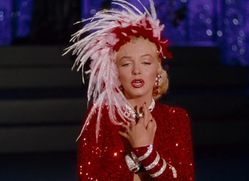Movie still from “Gentlemen Prefer Blondes” (1953), directed by Howard Hawks – A woman in a red and white outfit with a pink feather headdress; Close Up shot, Low angle