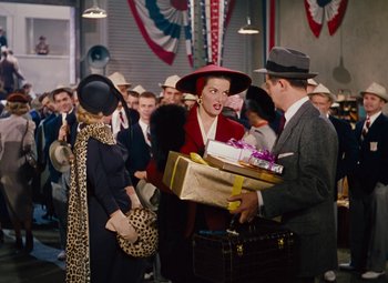 Movie still from “Gentlemen Prefer Blondes” (1953), directed by Howard Hawks – A group of people standing in a room with boxes; Wide shot, Over the shoulder angle