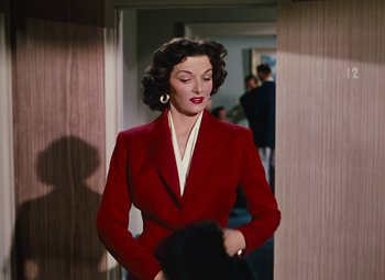 Movie still from “Gentlemen Prefer Blondes” (1953), directed by Howard Hawks – A woman in a red jacket standing in a hallway; Medium shot, Over the shoulder angle