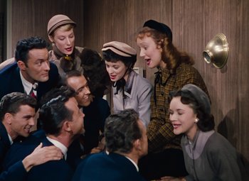 Movie still from “Gentlemen Prefer Blondes” (1953), directed by Howard Hawks – A group of men and women sitting around each other; Medium shot, Overhead angle