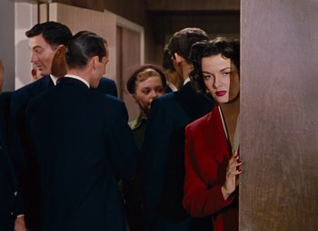 Movie still from “Gentlemen Prefer Blondes” (1953), directed by Howard Hawks – A woman in a red jacket standing next to a group of people; Medium shot, Over the shoulder angle
