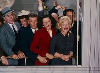 Movie still from “Gentlemen Prefer Blondes” (1953), directed by Howard Hawks – A group of people standing next to each other on a train; Wide shot, Low angle
