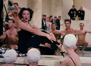 Movie still from “Gentlemen Prefer Blondes” (1953), directed by Howard Hawks – A group of men and women sitting on a wall; Wide shot, High angle