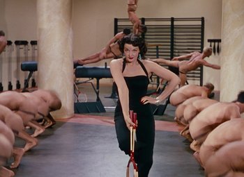 Movie still from “Gentlemen Prefer Blondes” (1953), directed by Howard Hawks – A woman holding a baseball bat in front of a group of naked men; Wide shot, High angle
