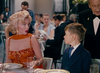 Movie still from “Gentlemen Prefer Blondes” (1953), directed by Howard Hawks – A woman and a young boy sitting at a dinner table; Medium shot, Over the shoulder angle