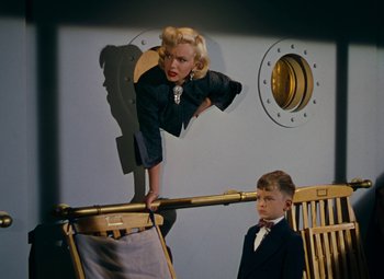 Movie still from “Gentlemen Prefer Blondes” (1953), directed by Howard Hawks – A woman and a boy are standing on a chair; Wide shot, Low angle