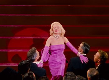 Movie still from “Gentlemen Prefer Blondes” (1953), directed by Howard Hawks – A woman in a purple dress is holding her hands up to her chest; Wide shot, Low angle