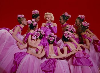 Movie still from “Gentlemen Prefer Blondes” (1953), directed by Howard Hawks – A group of women dressed in pink dresses and flowers; Wide shot, Low angle