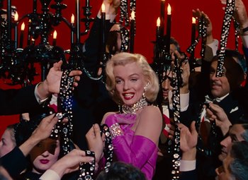 Movie still from “Gentlemen Prefer Blondes” (1953), directed by Howard Hawks – A woman in a purple dress surrounded by candles; Medium shot, Low angle