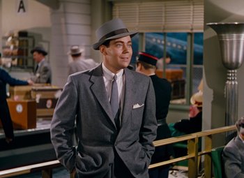 Movie still from “Gentlemen Prefer Blondes” (1953), directed by Howard Hawks – A man in a suit and hat standing next to other people; Medium shot, Over the shoulder angle