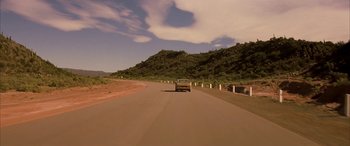 Movie still from “Gerry” (2002), directed by Gus Van Sant – A car driving down a road near a hill; Extreme Wide shot, Low angle