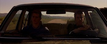 Movie still from “Gerry” (2002), directed by Gus Van Sant – Two men in the back seat of a car driving down a dirt road; Medium shot, Low angle