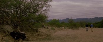 Movie still from “Gerry” (2002), directed by Gus Van Sant – A dirt field with trees and mountains in the background; Extreme Wide shot, High angle