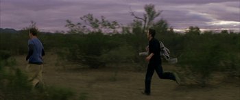 Movie still from “Gerry” (2002), directed by Gus Van Sant – A man is running in the grass with a frisbee; Wide shot, Over the shoulder angle