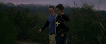 Movie still from “Gerry” (2002), directed by Gus Van Sant – Two young men are walking in a wooded area at dusk; Medium shot, Over the shoulder angle