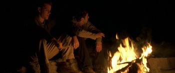 Movie still from “Gerry” (2002), directed by Gus Van Sant – Two men sitting in front of a fire at night; Medium shot, Low angle