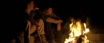Movie still from “Gerry” (2002), directed by Gus Van Sant – Two young men sitting next to each other in front of a fire; Medium shot, Low angle