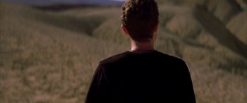 Movie still from “Gerry” (2002), directed by Gus Van Sant – A man standing in a field at night; Medium shot, Over the shoulder angle