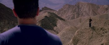 Movie still from “Gerry” (2002), directed by Gus Van Sant – A man standing on top of a mountain looking at the sky; Extreme Wide shot, High angle