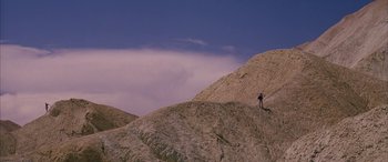 Movie still from “Gerry” (2002), directed by Gus Van Sant – A person standing on top of a hill; Extreme Wide shot, Low angle