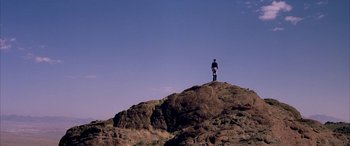 Movie still from “Gerry” (2002), directed by Gus Van Sant – A man standing on top of a hill looking at the sky; Extreme Wide shot, Low angle