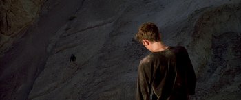 Movie still from “Gerry” (2002), directed by Gus Van Sant – A young man standing on top of a hill looking at another man; Wide shot, Low angle