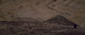Movie still from “Gerry” (2002), directed by Gus Van Sant – A large rock formation in the middle of the desert; Extreme Wide shot, High angle
