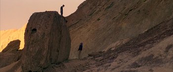 Movie still from “Gerry” (2002), directed by Gus Van Sant – Two people standing on a rock formation on a hill; Extreme Wide shot, Low angle