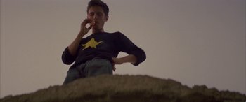 Movie still from “Gerry” (2002), directed by Gus Van Sant – A man sitting on top of a hill while smoking a cigarette; Medium shot, Overhead angle