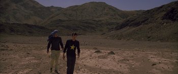 Movie still from “Gerry” (2002), directed by Gus Van Sant – Two people walking in the desert near a mountain; Wide shot, Over the shoulder angle