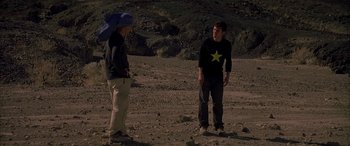 Movie still from “Gerry” (2002), directed by Gus Van Sant – Two people standing in the dirt talking to each other; Wide shot, Over the shoulder angle