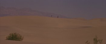 Movie still from “Gerry” (2002), directed by Gus Van Sant – A couple of people walking across a sand dune; Extreme Wide shot, High angle