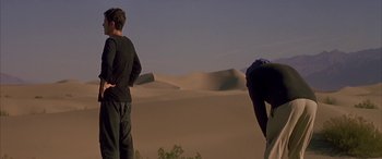 Movie still from “Gerry” (2002), directed by Gus Van Sant – Two men standing in the desert looking at the sand dunes; Wide shot, Low angle