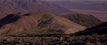 Movie still from “Gerry” (2002), directed by Gus Van Sant – Two people are standing on a hill in the middle of the desert; Extreme Wide shot, High angle