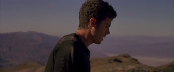 Movie still from “Gerry” (2002), directed by Gus Van Sant – A young man standing on top of a hill with mountains in the background; Close Up shot, Low angle