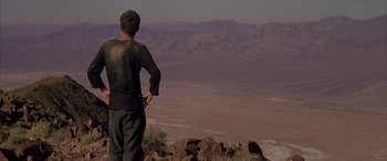 Movie still from “Gerry” (2002), directed by Gus Van Sant – A man standing on top of a hill looking at the mountains; Wide shot, Low angle