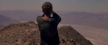 Movie still from “Gerry” (2002), directed by Gus Van Sant – A man standing on top of a mountain looking at the sky; Wide shot, Low angle