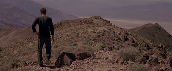 Movie still from “Gerry” (2002), directed by Gus Van Sant – A man standing on a rocky hill looking at the sky; Wide shot, Low angle