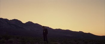 Movie still from “Gerry” (2002), directed by Gus Van Sant – A person standing in a field with a mountain in the background; Wide shot, Low angle