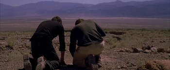 Movie still from “Gerry” (2002), directed by Gus Van Sant – Two men kneeling down on the ground in the desert; Wide shot, Low angle