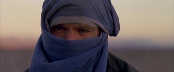 Movie still from “Gerry” (2002), directed by Gus Van Sant – A man wearing a blue head covering and a gray hat; Close Up shot, Low angle