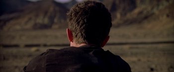 Movie still from “Gerry” (2002), directed by Gus Van Sant – A man sitting in front of a mountain range; Close Up shot, Over the shoulder angle