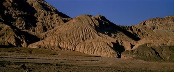 Movie still from “Gerry” (2002), directed by Gus Van Sant – A mountain with a lot of sand on top of it; Extreme Wide shot, Low angle