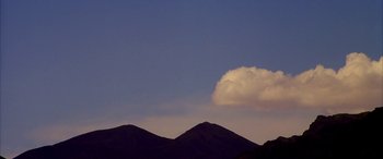 Movie still from “Gerry” (2002), directed by Gus Van Sant – A white cloud sitting on top of a mountain; Extreme Wide shot, Low angle