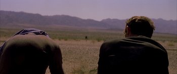 Movie still from “Gerry” (2002), directed by Gus Van Sant – Two people sitting in a field looking out at a bison in the distance; Close Up shot, Over the shoulder angle